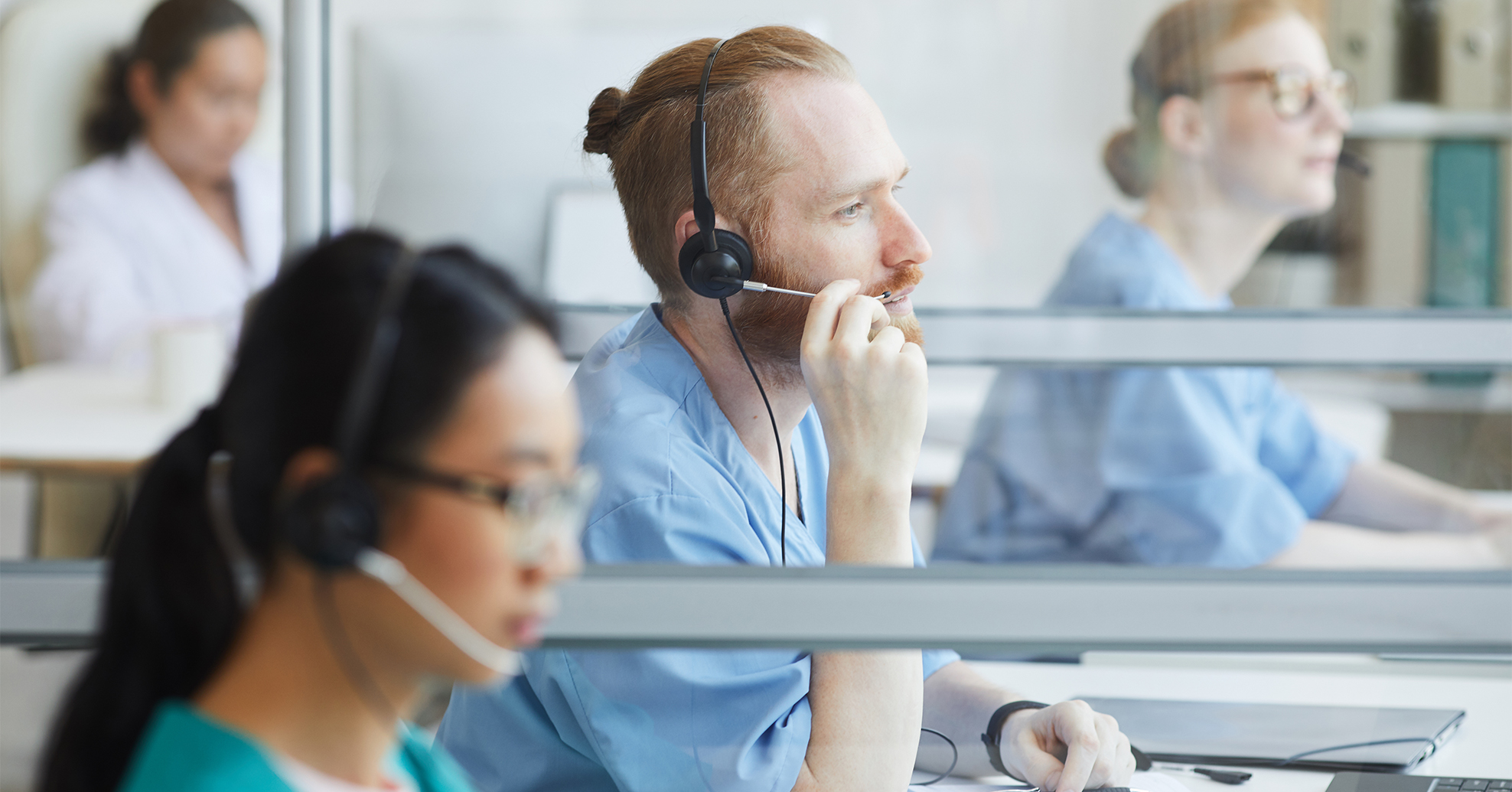 Healthcare contact center agent using a headset and computer in a busy office environment.