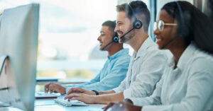 Two customer service agents wearing headsets sitting at desks in a contact center.